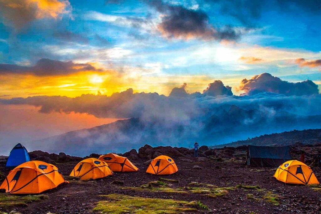 Orange tents pitched on a rocky mountain campground at sunset with dramatic blue sky and clouds